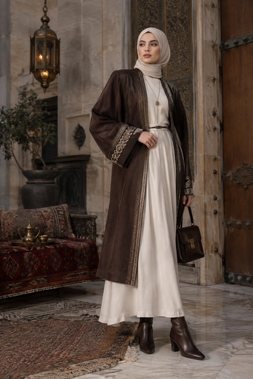 Elegant Brown Coat and Cream Dress A woman wearing a cream maxi dress, beige hijab, and long brown embroidered coat with brown ankle boots and a structured handbag.