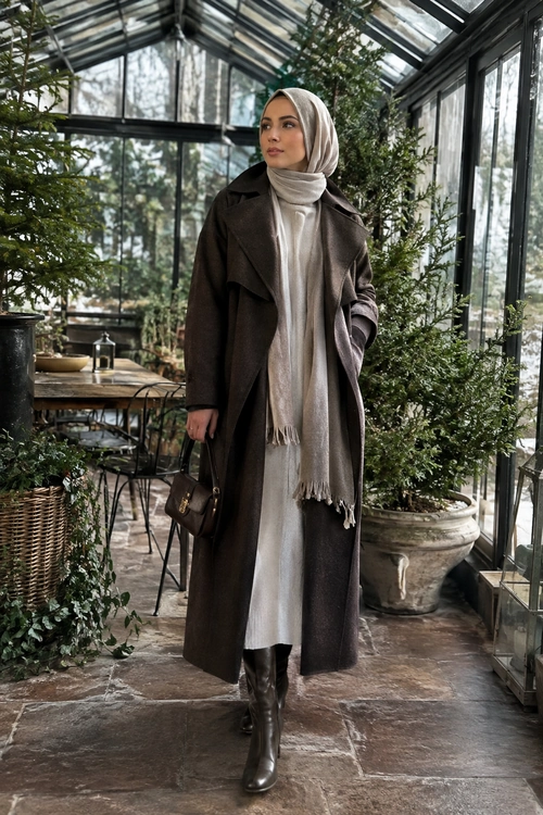 Elegant Brown Coat and Scarf Look A woman wears a long brown coat over a light dress with a taupe headscarf, dark knee-high boots, and a small handbag.