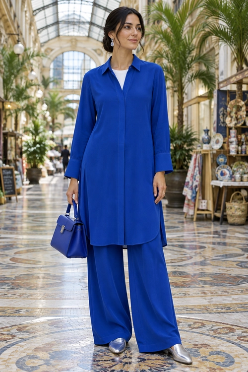 Cobalt Blue Tunic and Wide-Leg Trousers A woman wears a cobalt blue tunic with matching wide-leg trousers, silver shoes, and a structured blue handbag.
