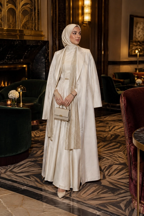 Elegant Ivory Modest Look A woman wears an ivory hijab, long flowing dress, tailored coat, scarf, pointed shoes, and a small structured handbag.