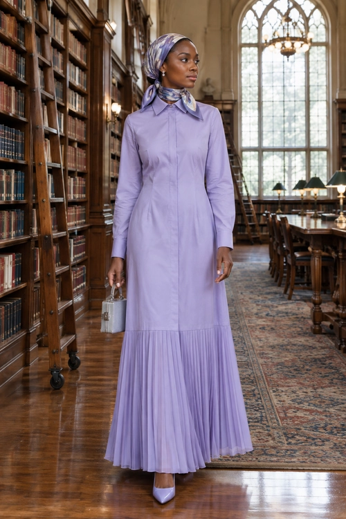 A woman wears a long lavender collared dress with a pleated skirt, patterned headscarf, pointed-toe heels, and a small silver handbag.
