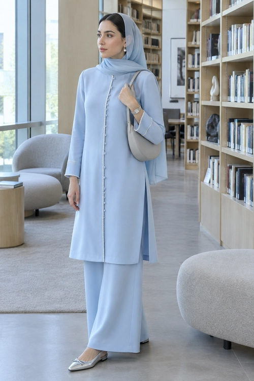 Light Blue Modest Tunic Outfit A woman wears a light blue long tunic with decorative front trim, matching long bottoms, a coordinating headscarf, silver pointed flats, and a taupe shoulder bag.