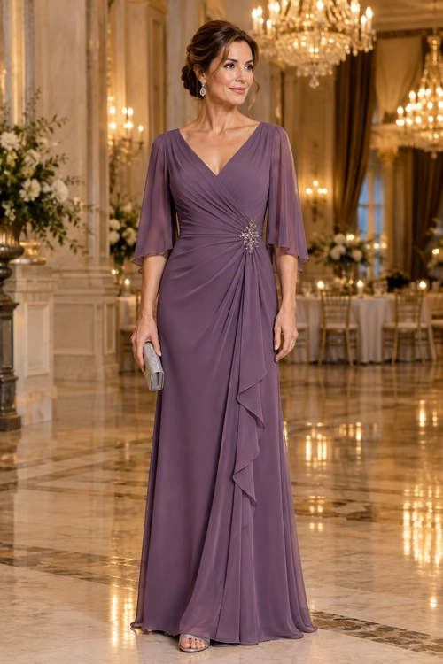 A woman wears a floor-length mauve gown with sheer flutter sleeves, a draped wrap bodice, and a jeweled waist detail, paired with a silver clutch, earrings, and open-toe sandals.