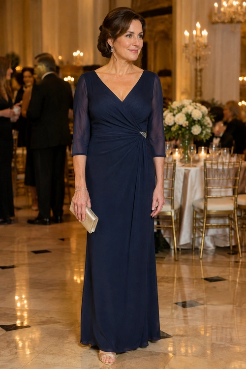 A woman wears a floor-length navy gown with sheer three-quarter sleeves, a gathered waist and a gold clutch.