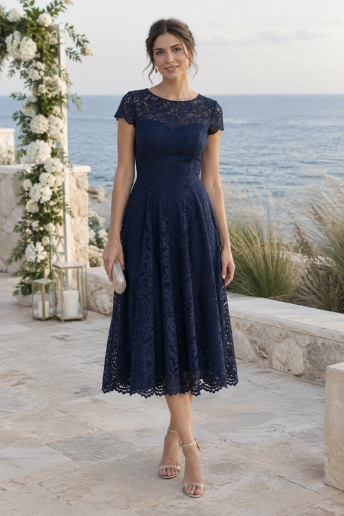 Navy Lace Midi Dress A woman wears a navy lace midi dress with short sleeves and nude strappy heels beside the sea.
