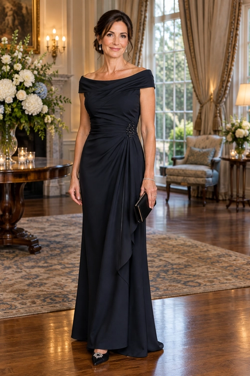 Navy Off-Shoulder Gown A woman wears a floor-length navy off-shoulder gown with a draped skirt, jeweled waist detail, black clutch, and embellished heels.