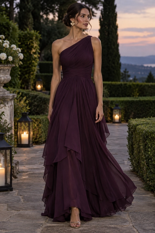 Plum One-Shoulder Evening Gown A woman wears a flowing plum one-shoulder gown with layered ruffles, gold floral earrings, and strappy sandals.