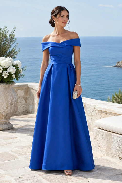 A woman wears a floor-length royal blue off-shoulder gown with a full skirt, a small clutch, a bracelet, and sandals.