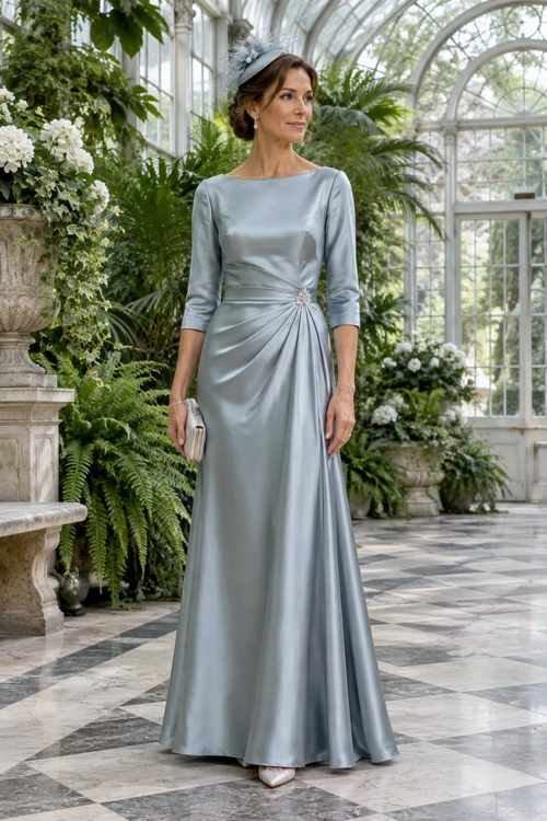 A woman wears a pale silver-blue satin gown with three-quarter sleeves, a draped waist, and a matching feathered headpiece.